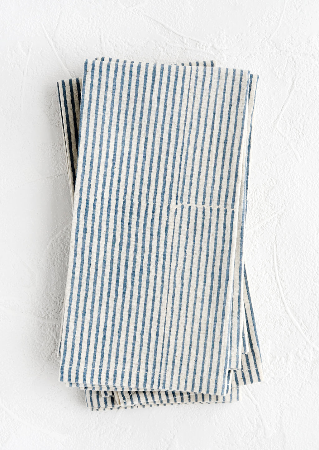 Indigo Stripe: A stack of folded fabric napkins in natural cotton with hand-drawn line pattern in indigo.