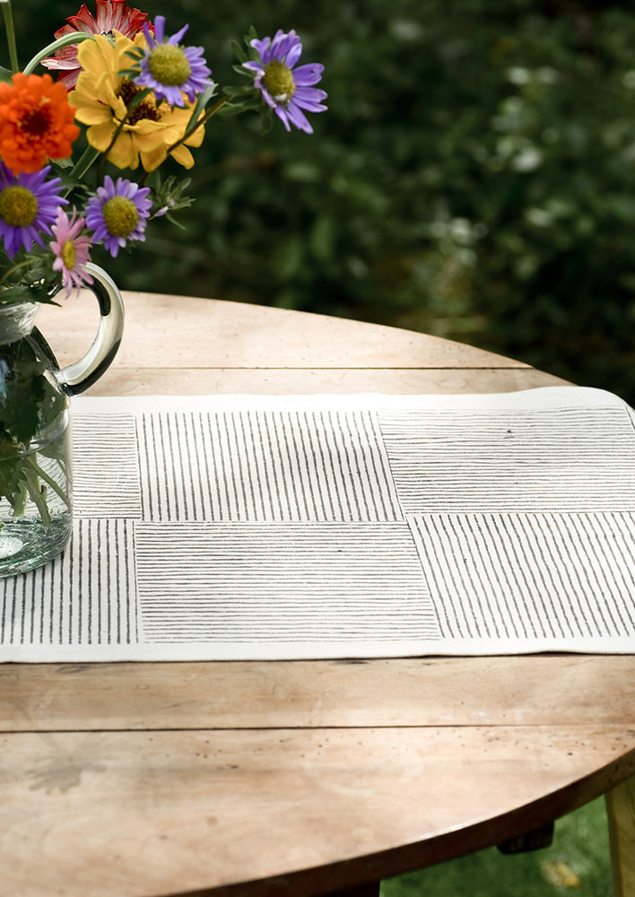 A natural cotton table runner with black broken stripe block print.