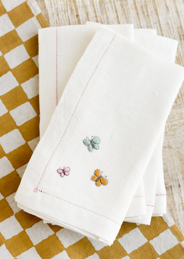 White linen napkins with pastel colored butterfly embroidery.