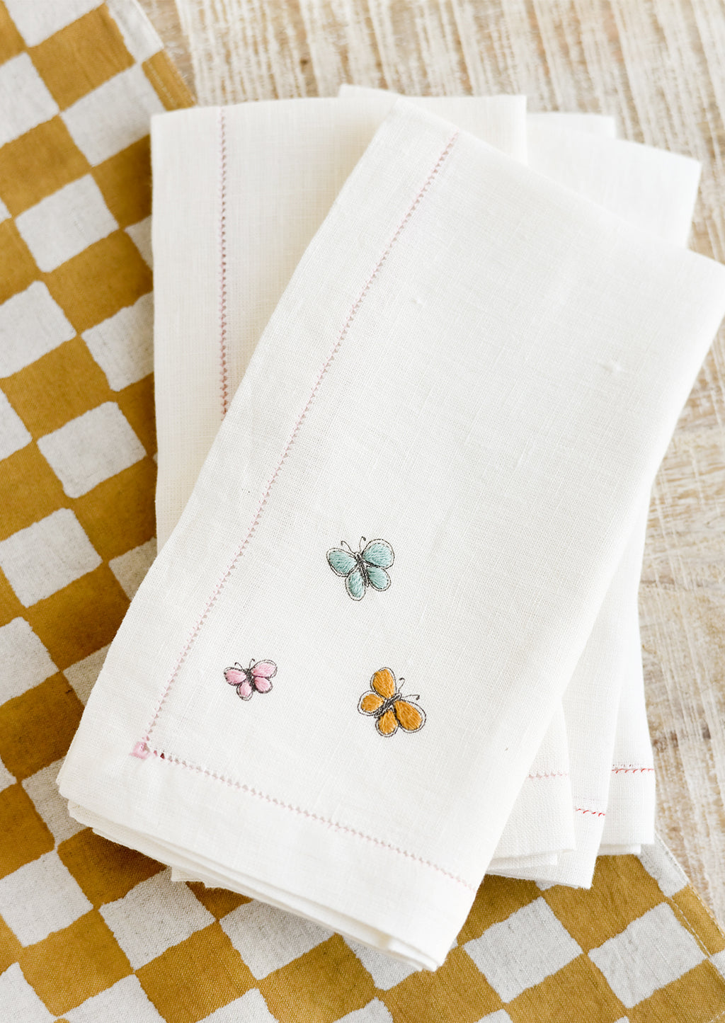 Pastel Multi: White linen napkins with pastel colored butterfly embroidery.