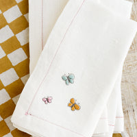 Pastel Multi: White linen napkins with pastel colored butterfly embroidery.