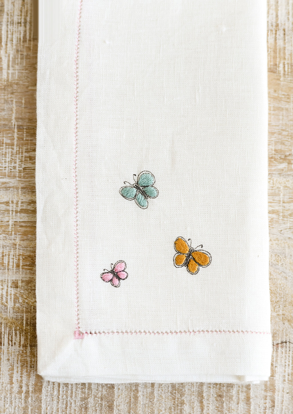 3: Butterfly embroidery detailing on a white linen napkin.