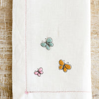3: Butterfly embroidery detailing on a white linen napkin.