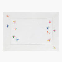2: A white linen placemat with multicolor bee embroidery.