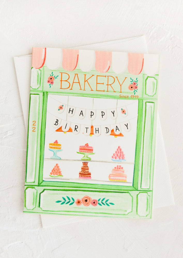 A birthday card with illustration of a bakery window filled with cakes and flag reading "Happy birthday".