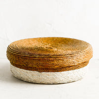 Ochre: A shallow, round storage basket with lid, woven from dried palm leaf in two-tone design.