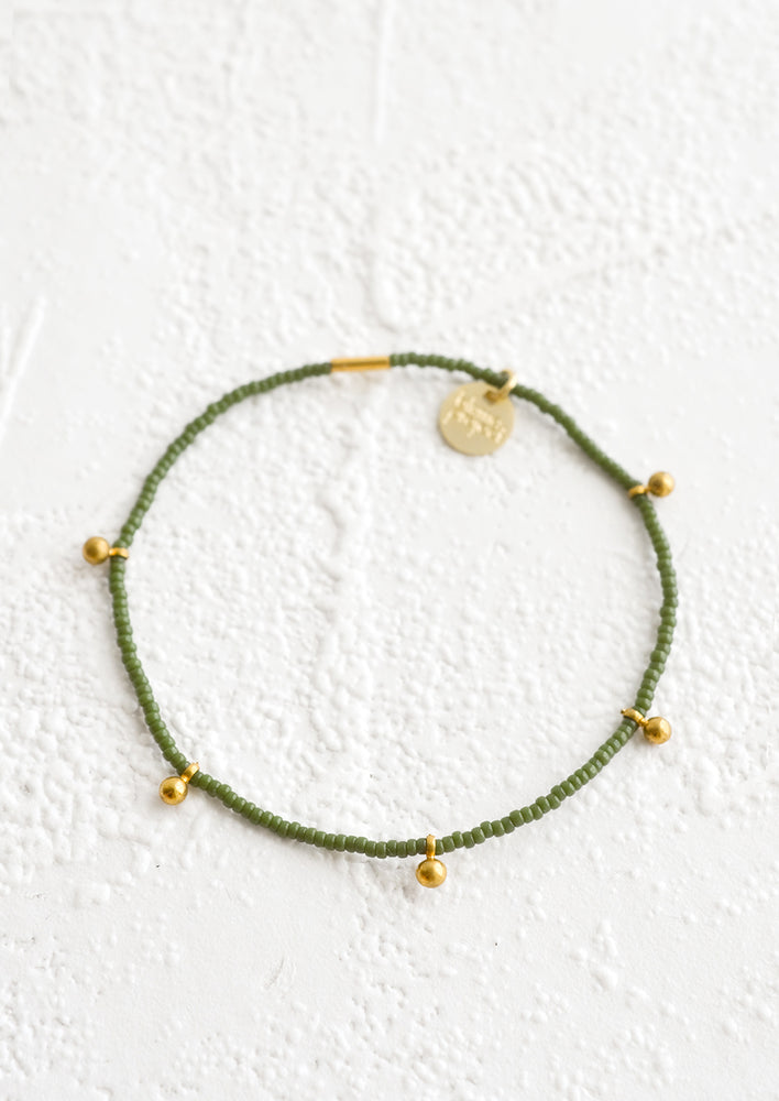 Bracelet made from olive colored glass seed beads with brass ball accent charms and logo tag