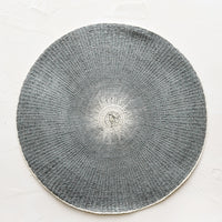 Dark Grey: A round straw placemat in dark grey with white spot at center.