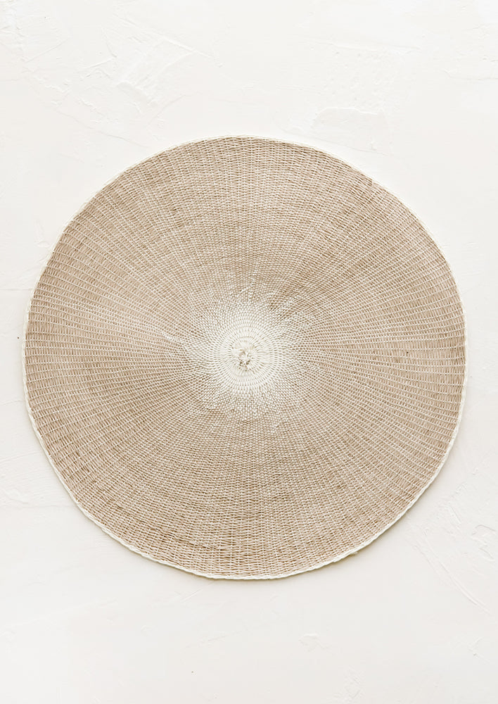 A round straw placemat in taupe with white spot at center.
