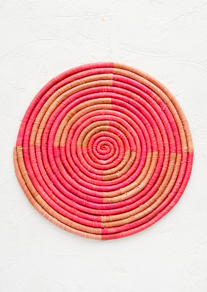 1: A round trivet made from woven raffia in two shades of pink.