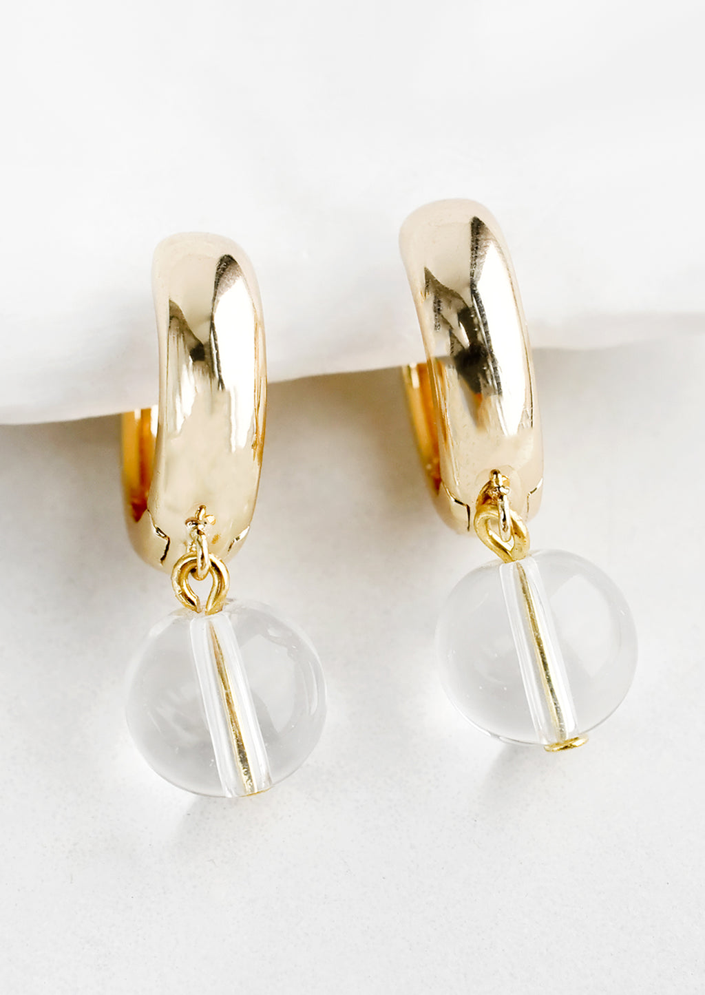 Clear: A pair of gold huggie hoop earrings with single spherical clear bead detail.