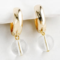 Clear: A pair of gold huggie hoop earrings with single spherical clear bead detail.