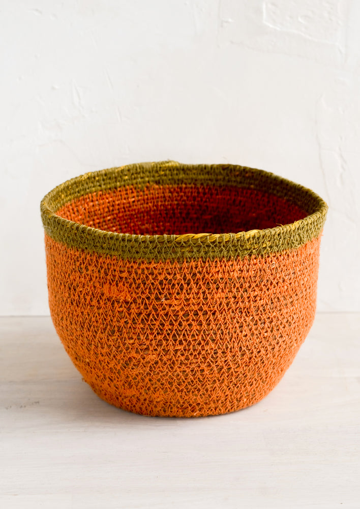 Small / Coral: A round seagrass storage basket in coral color with ochre stripe around top.
