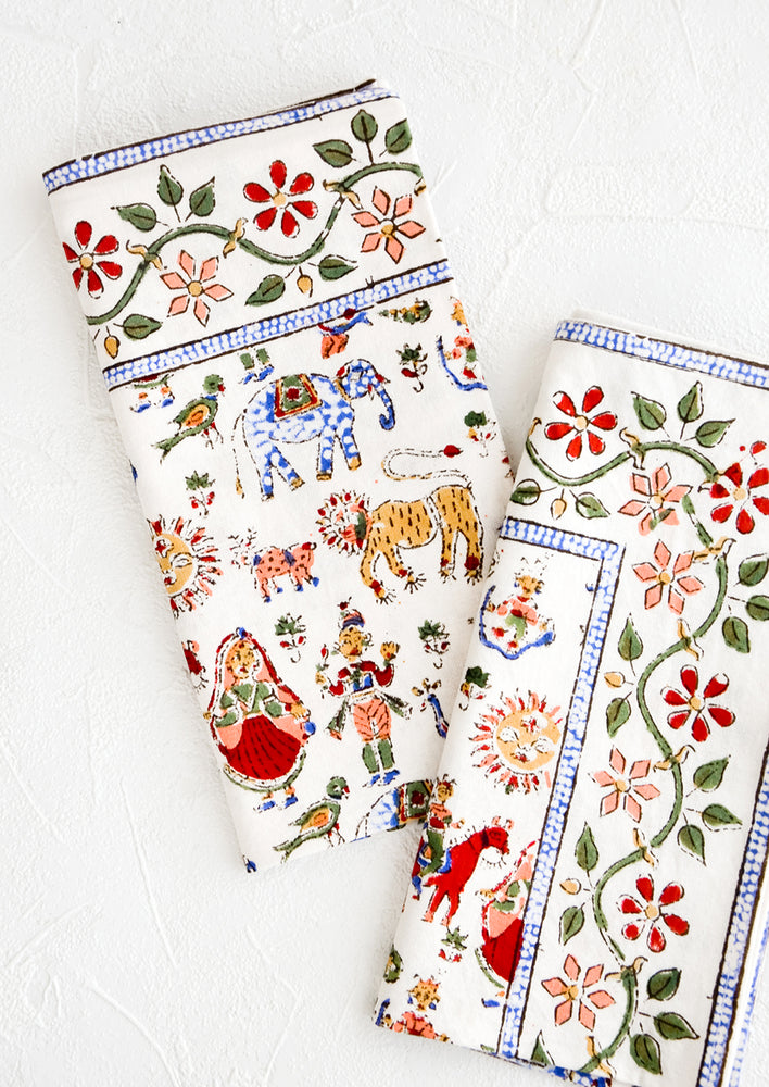 Pair of folded cotton dinner napkins in white with multicolor carnival print