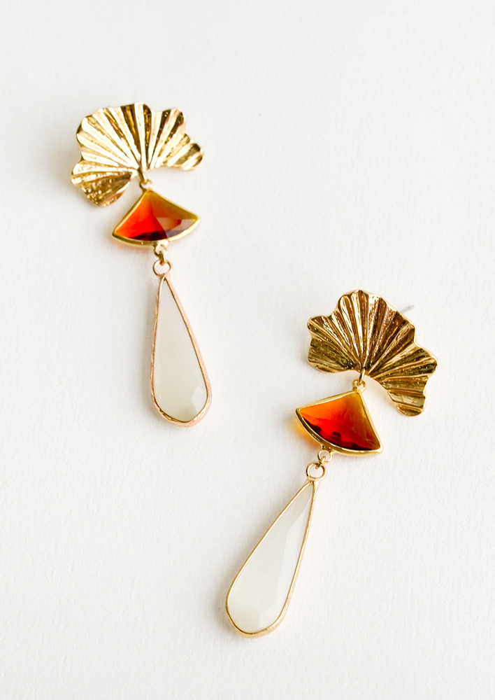1: Dangling earrings featuring red triangle and ivory teardrop crystals hanging from a yellow gold shell charm.