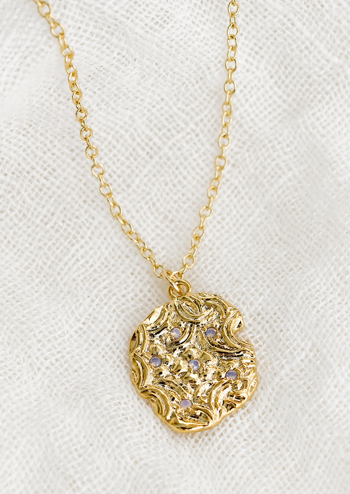 A textured, wax like gold charm with opal detailing on gold chain.