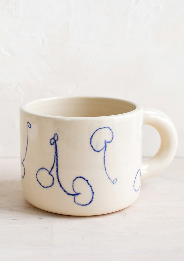 An ivory ceramic mug with line drawing cherries in blue.