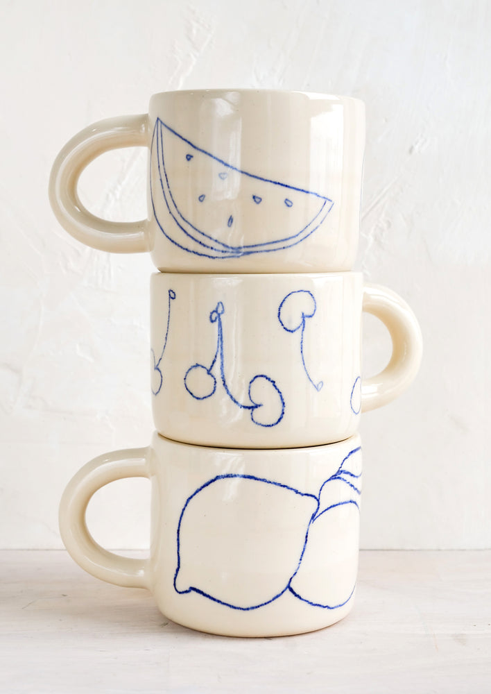 2: A stack of three ceramic mugs with fruit line drawings.