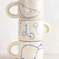 2: A stack of three ceramic mugs with fruit line drawings.