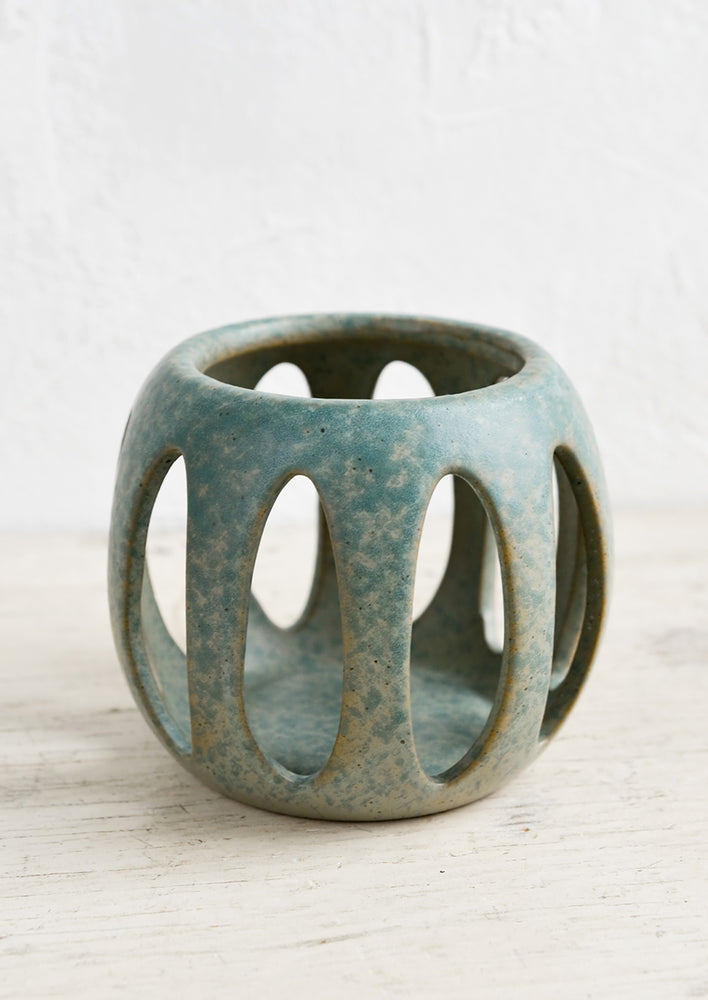 A blue-green ceramic votive holder with petal-shaped cutouts.