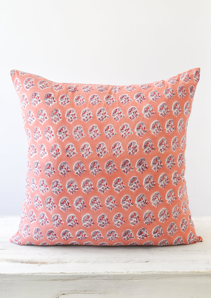 A square block printed pillow with a pink, grey, and red floral design.
