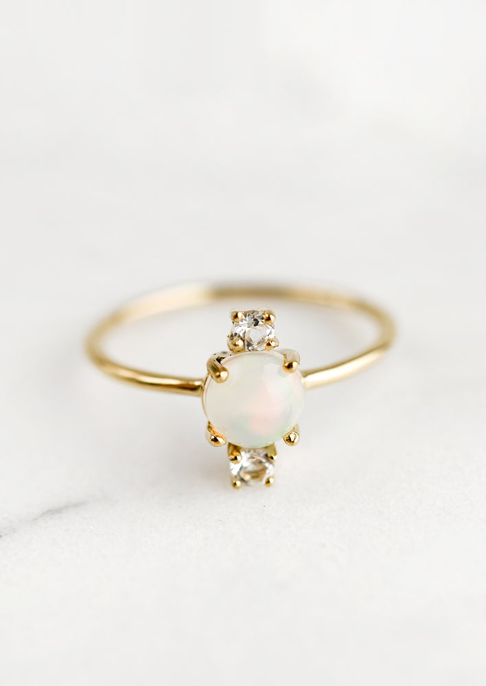 A gold ring with large center opal stone and two small white topaz stones.