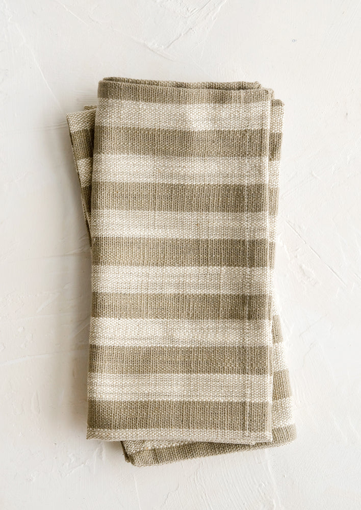A pair of folded napkins in tan with wide ivory stripes throughout.