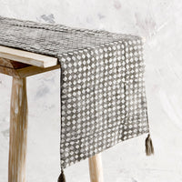 1: Table runner shown on a console table. Distressed grey with white stamped diamond print and tassels at corners.