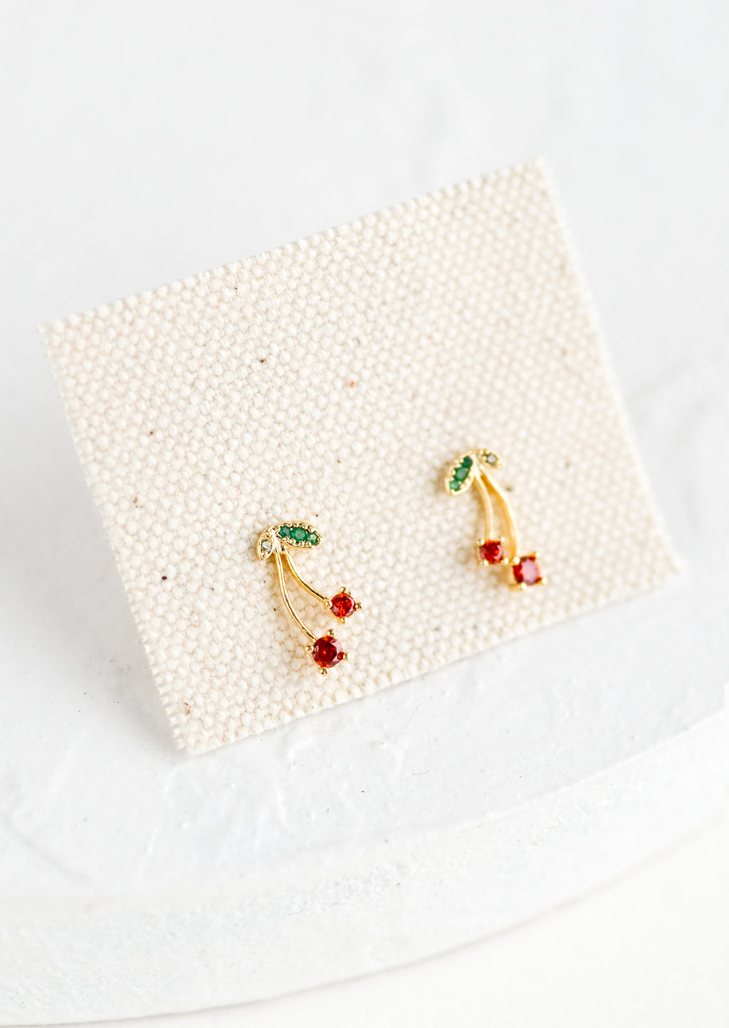 2: A pair of gold stud earrings on canvas square.