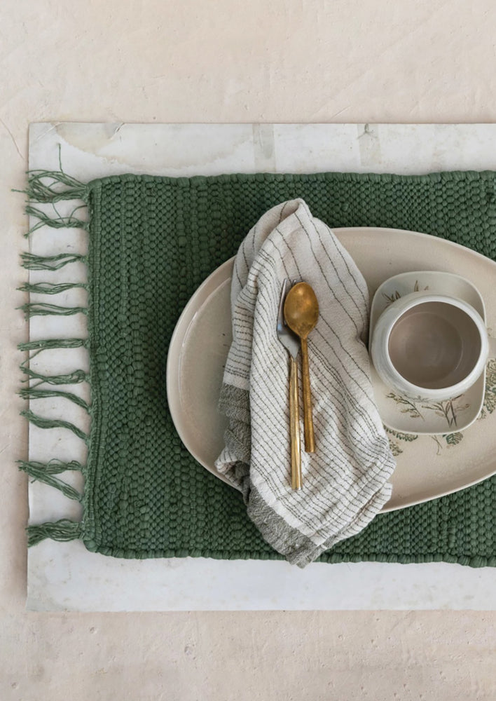 An olive green chindi weave placemat styled with spoons and ceramics.