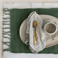 2: An olive green chindi weave placemat styled with spoons and ceramics.
