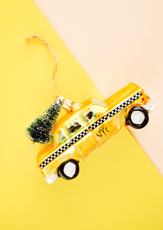 A glass ornament in the shape of a yellow cab with christmas tree on roof.