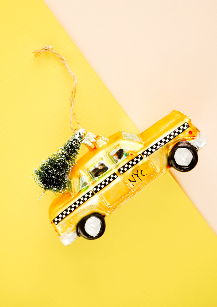 A glass ornament in the shape of a yellow cab with christmas tree on roof.