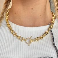 3: A woman wearing a gold chainlink necklace with toggle closure at front and center.