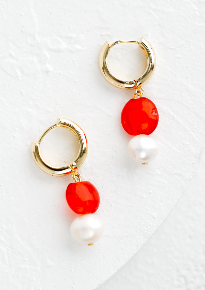 A pair of earrings with gold huggie top and red glass and pearl bead.