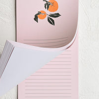 2: A light pink lined notepad with two oranges at the top