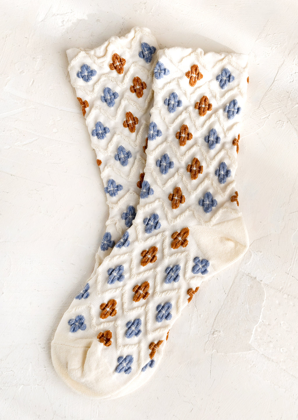 1: A pair of ivory socks with raised diamond texture and blue and brown clover shapes.