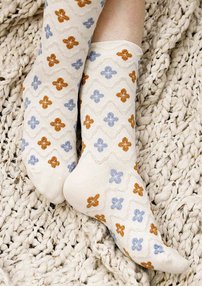 A pair of ivory socks with raised diamond texture and blue and brown clover shapes.