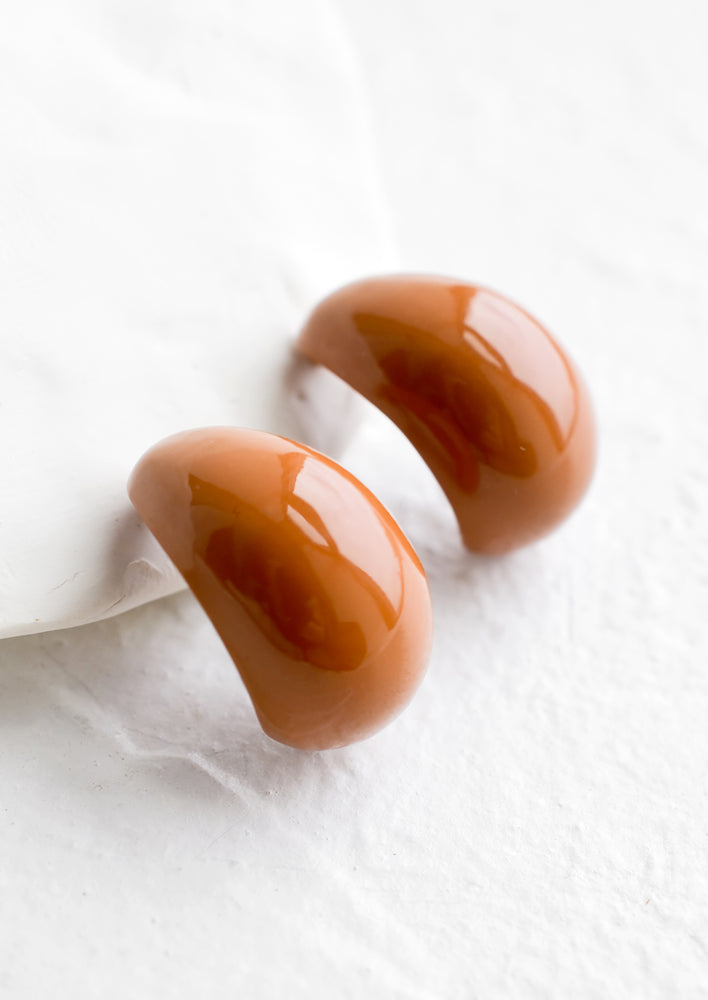 A pair of glossy brown bean shaped earrings.