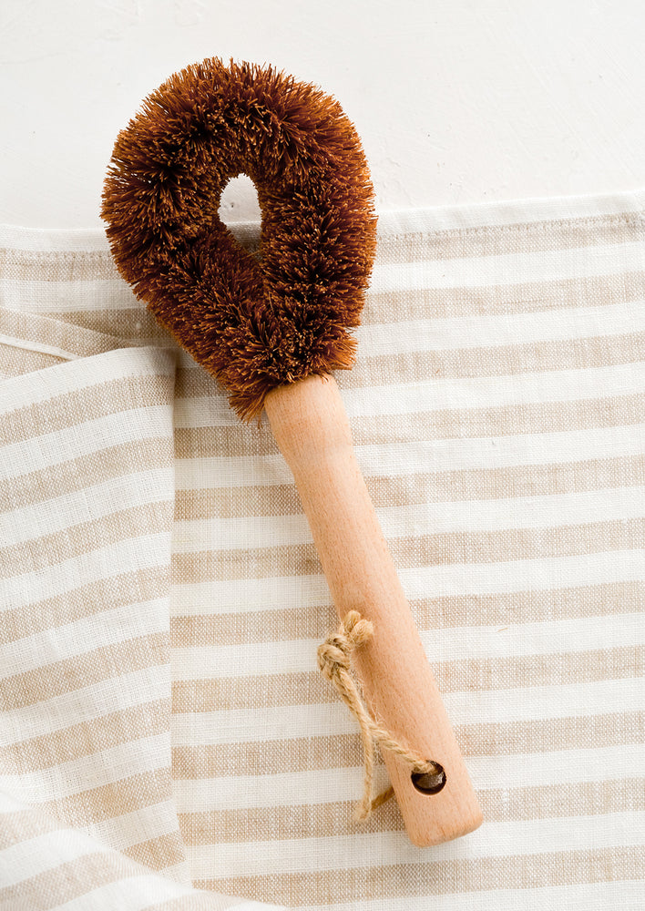 A coconut fiber dish brush with wooden handle.