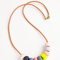 Cool Glow: Woven leather cord necklace with gold clasp and rounded clay beads tans, pinks,gray, blue, and neon yellow.