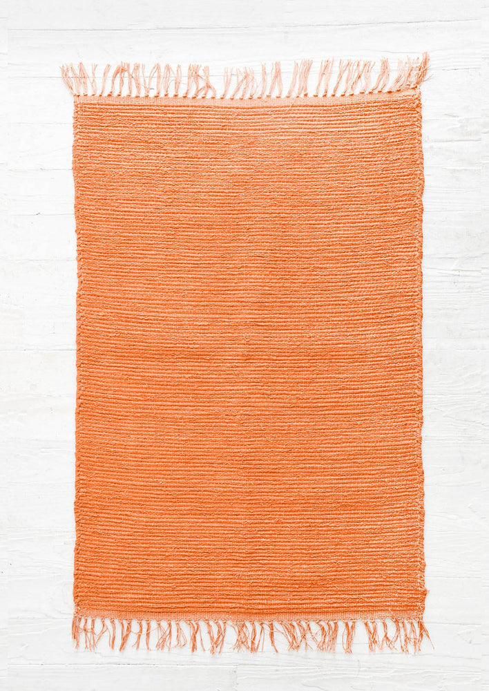 Cotton flatweave rug in solid color red orange with slight texture, fringe trim on two ends
