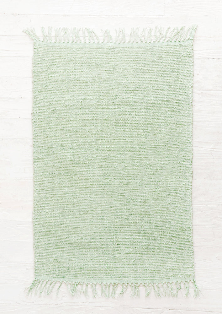 Lagos: Cotton flatweave rug in solid mint green color with slight texture, fringe trim on two ends