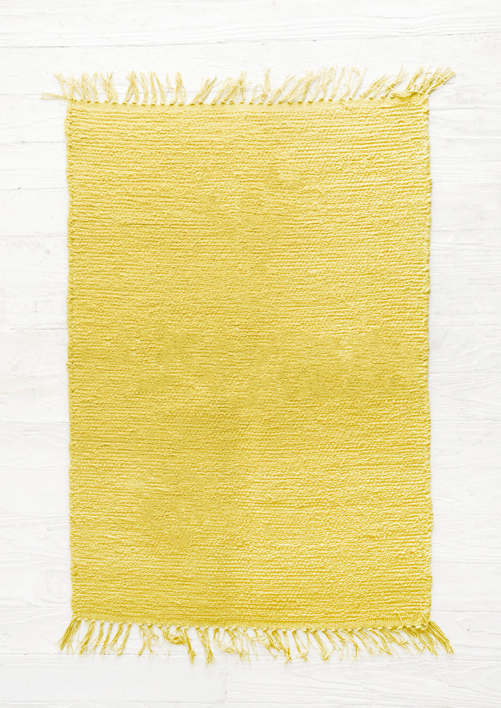 Sulfur: Cotton flatweave rug in solid color yellow green with slight texture, fringe trim on two ends
