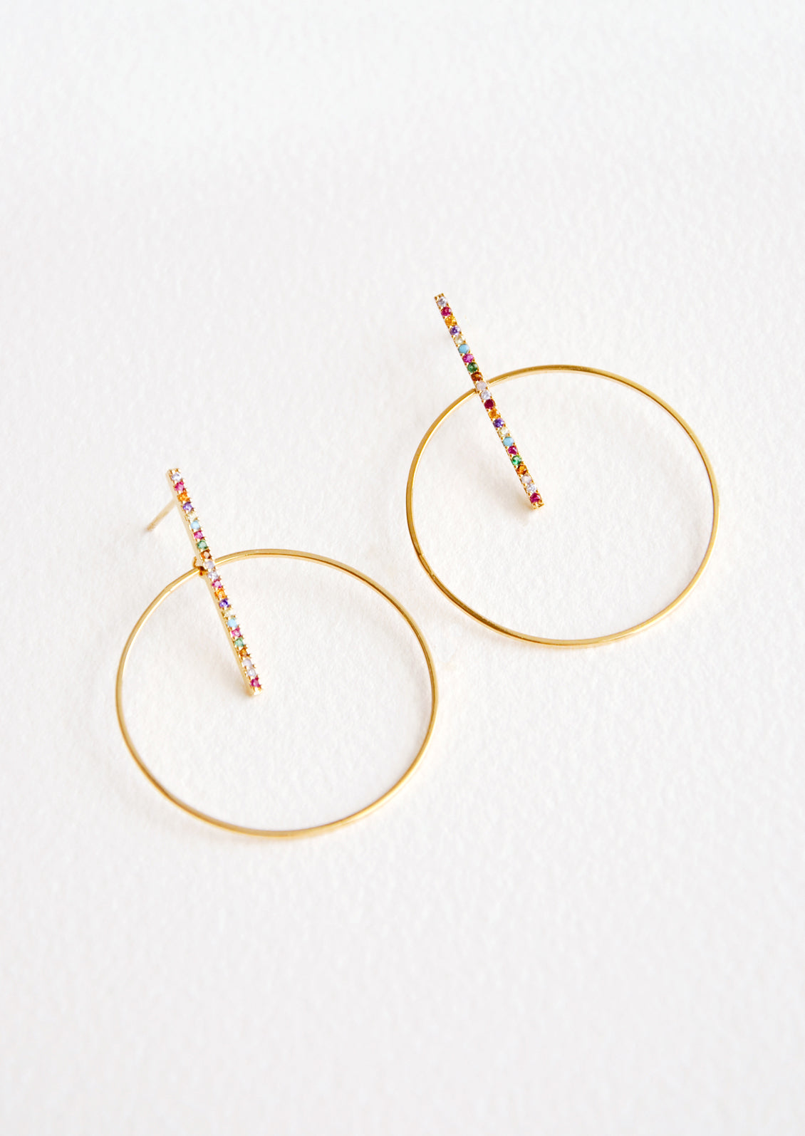 Round gold circle earrings with post across center of circle, featuring colored crystals