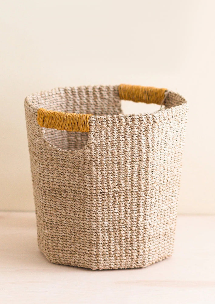 An octogonal natural basket with mustard wrapped cutout handle.