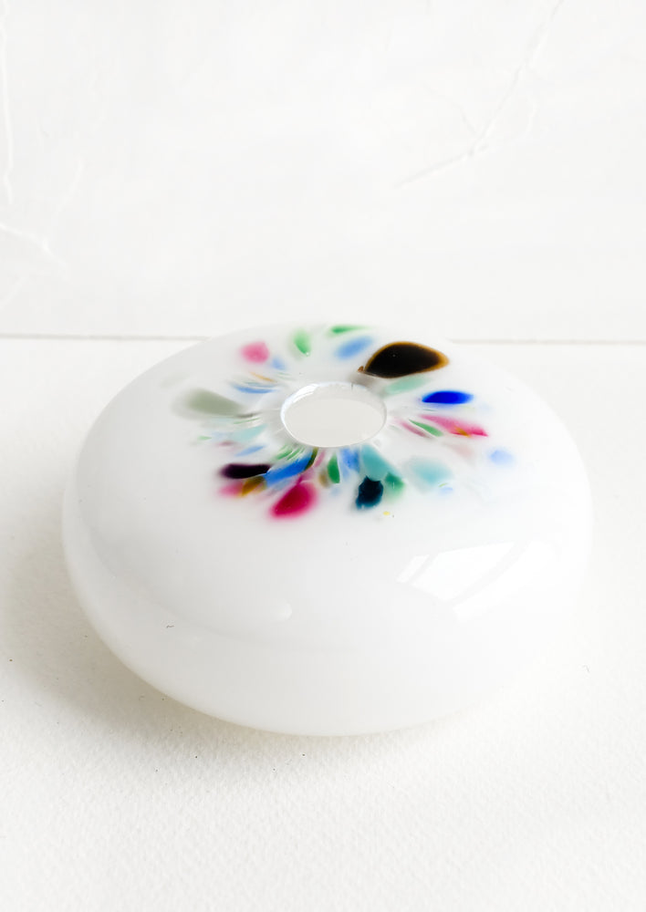 A glass bud vase in white with colorful fleck detail around opening.