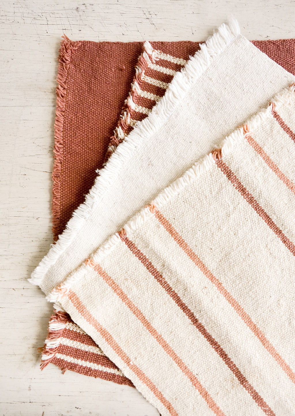 1: Four natural cotton placemats with frayed edges in a palette of cream, blush and terracotta