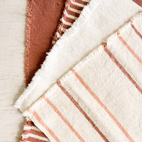 1: Four natural cotton placemats with frayed edges in a palette of cream, blush and terracotta