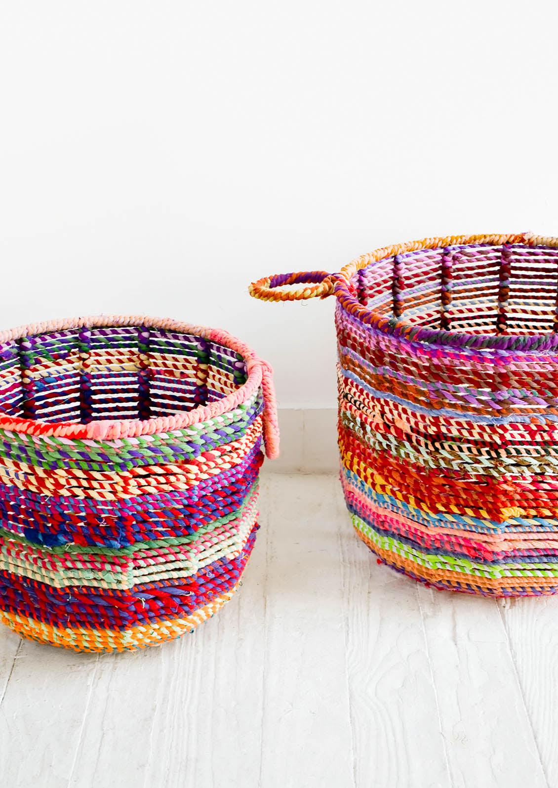 Round, circular storage bin made from colorful recycled fabrics woven together, featuring round handles at top.